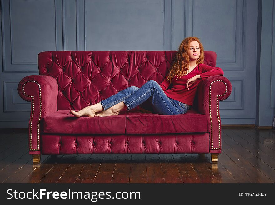 Young rich woman lying on red couch