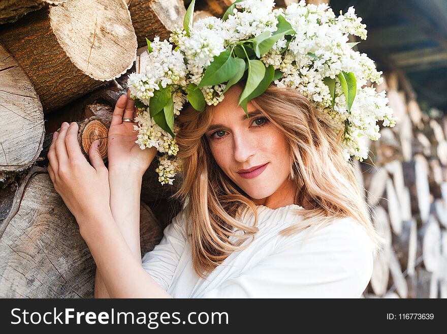 Portrait of young woman in lilac wreath. Girl with lilac flowers on head looking at camera smiling