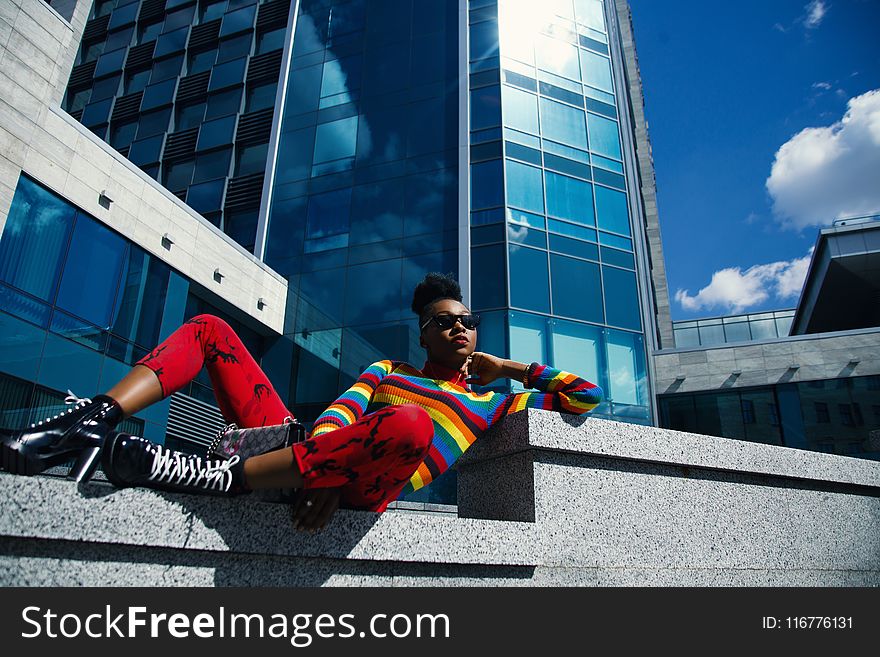 Woman In Multicolored Striped Long-sleeved Top Sitting On Gray Concrete Fence Near Building