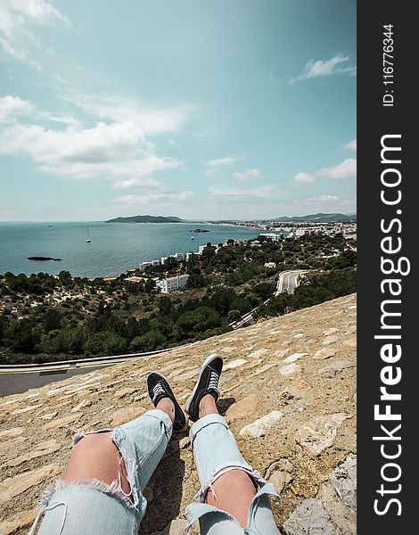 Man In Blue Tattered Jeans Sitting On Top Of The Mountain