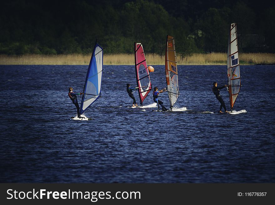 Four Person Riding Wind Sailboard on Body of Water