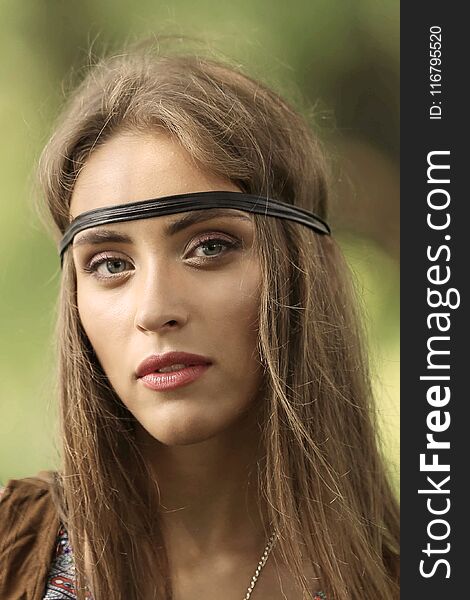 Portrait of a beautiful girl - a hippie with a headband on the background of the Park