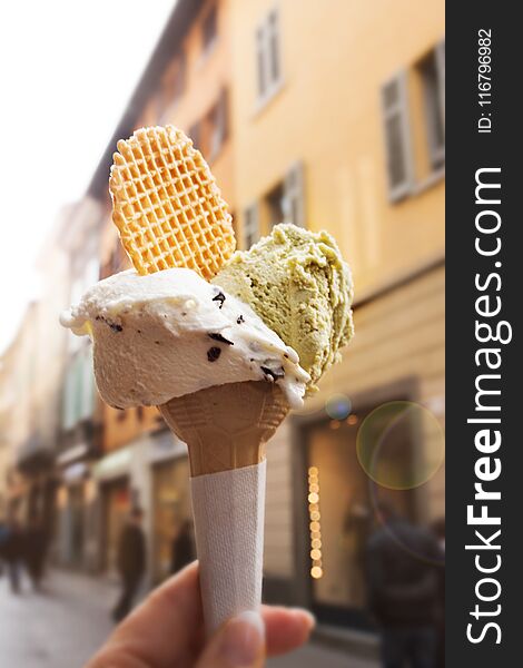 Ice cream cone with hand in summer with city scenery and short depth of field. Ice cream cone with hand in summer with city scenery and short depth of field