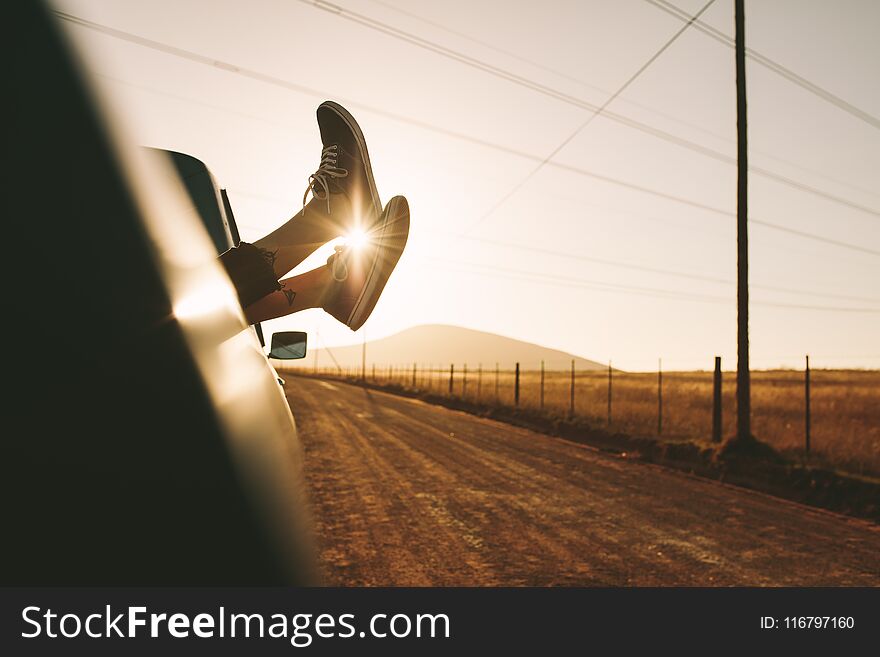 Legs of a woman relaxing at the back of a pick up truck on a highway in country side. Legs hanging out from car with sun in the background. Legs of a woman relaxing at the back of a pick up truck on a highway in country side. Legs hanging out from car with sun in the background.
