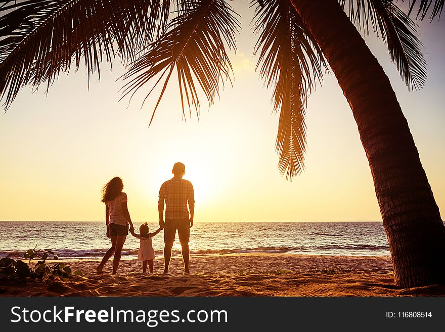 Family with one child stands against sunset sea beach and palms. Tropical vacations concept. Family with one child stands against sunset sea beach and palms. Tropical vacations concept