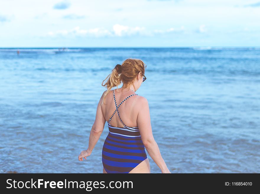 Woman Wearing Blue Monokini Standing Beside Body Of Water Under Blue Sky