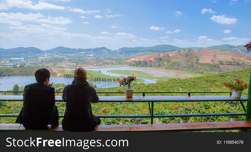 Two Men Sitting On Table Facing Lake