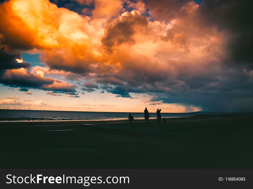 Silhouette Of People On Shore Under Cloudy Sky