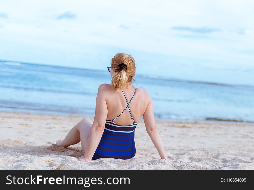 Woman Sits on White Sand Beach