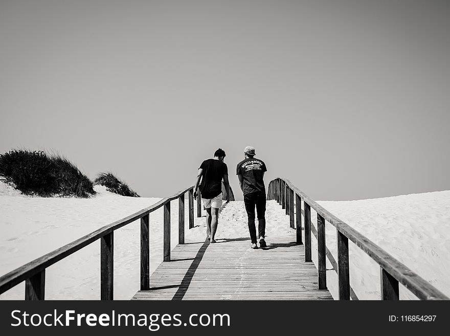 Grayscale Photography of Man and Woman Crossing Bridge