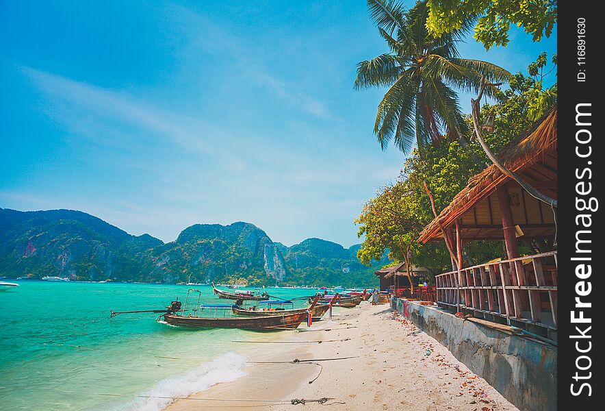 Wonderful scenery the cozy local village and the ocean shore with fishing boats on the limestone cliffs background. Idyllic place for the rest and relax. Phi Phi islands, the Kingdom of Thailand. Wonderful scenery the cozy local village and the ocean shore with fishing boats on the limestone cliffs background. Idyllic place for the rest and relax. Phi Phi islands, the Kingdom of Thailand.