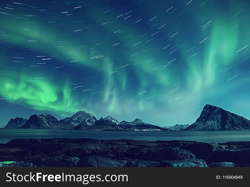 Northern Lights, Aurora Borealis shining green in night starry sky with star tracks at winter Lofoten Islands, Norway. Northern Lights, Aurora Borealis shining green in night starry sky with star tracks at winter Lofoten Islands, Norway