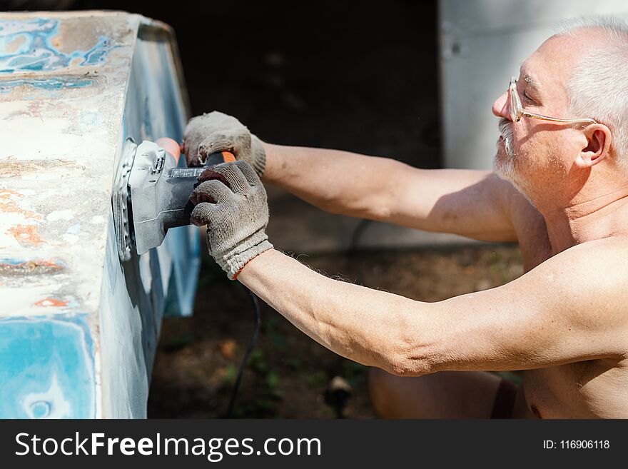 Older man is repairing and grinding an old boat with a grinder