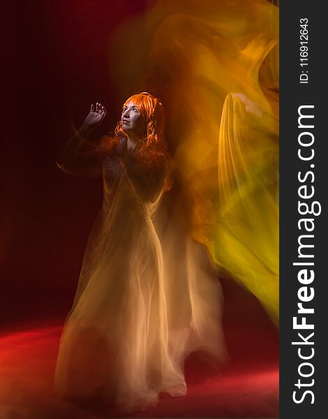 Old female actress with orange hair dancing in white dress with light show with yellow, orange and green lights around