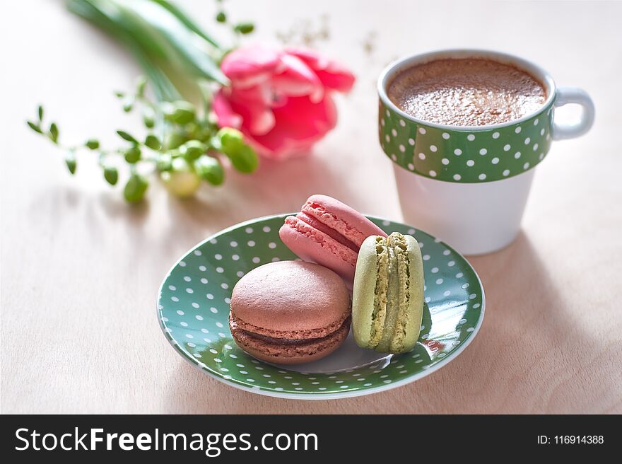 Spring coffee background. Pink tulip, freesia, espresso and macarons in front, spring flowers in the back.