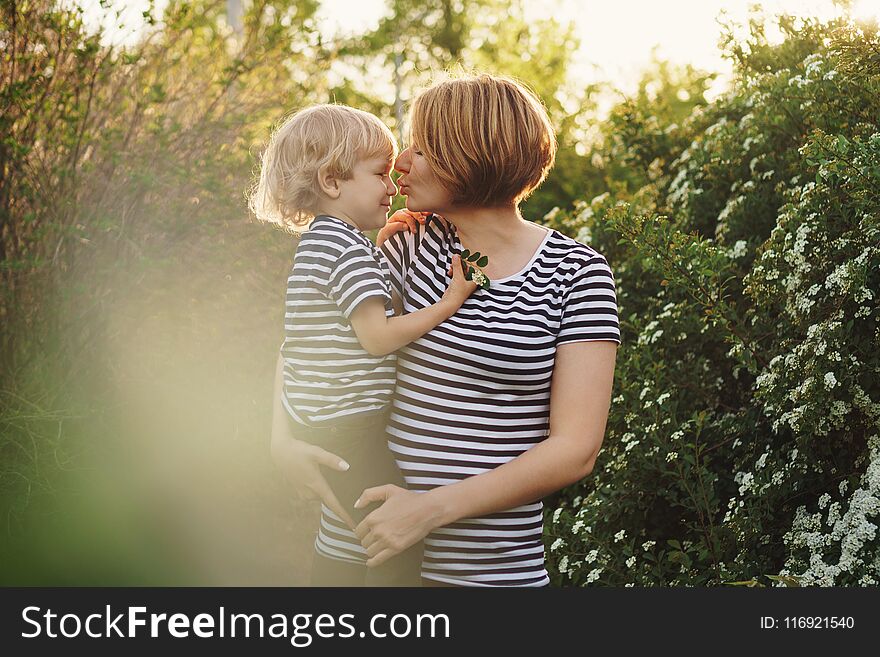 Mother and son in striped T-shirts. Woman holds boy in her arms and kisses him in nose. Family time. Mother and son in striped T-shirts. Woman holds boy in her arms and kisses him in nose. Family time
