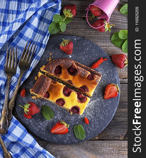 Two pieces of cheesecake with strawberries on a black graphite plate, top view, next to fresh ripe berries