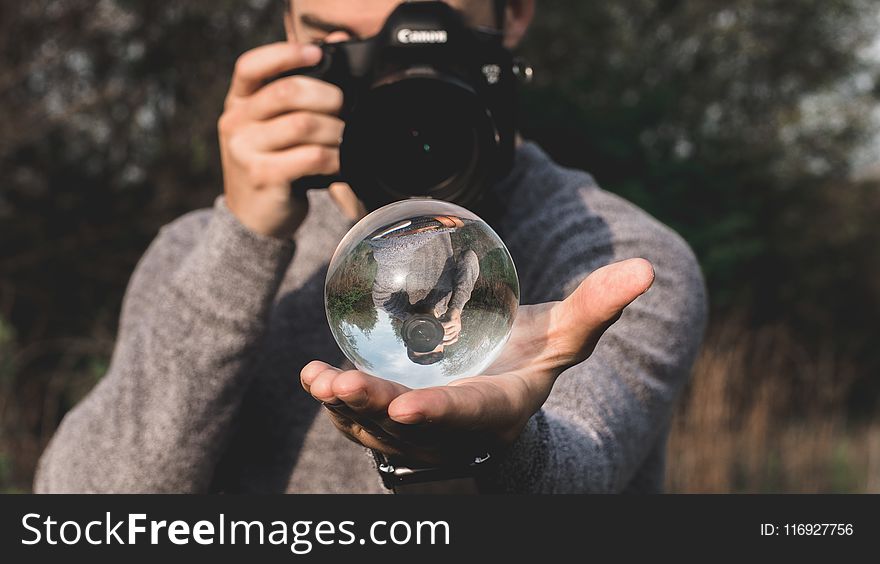 Man Wearing Space-dyed Sweater Holding Water Globe While Holding Black Canon Camera