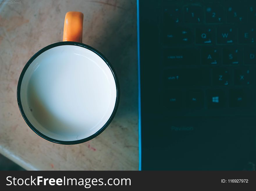 Orange and Black Ceramic Mug With Milk Beside Black Laptop