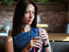 Close Up Of Beautiful Adult Brunette Woman In Jeans Dress Drinking Ice Tea From Glass Cup With Straw At Cafe Royalty Free Stock Images