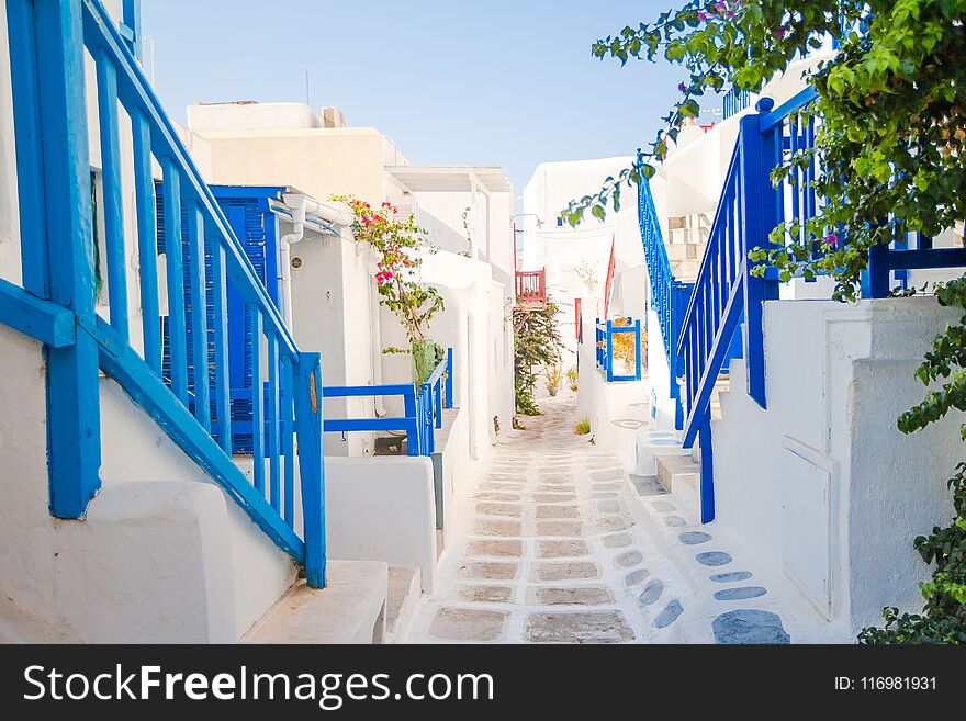 The narrow streets of greek island with blue balconies, stairs and flowers. Beautiful architecture building exterior with cycladic style. The narrow streets of greek island with blue balconies, stairs and flowers. Beautiful architecture building exterior with cycladic style.