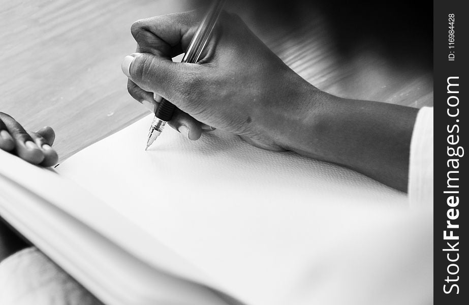 Grayscale Photography Of A Person Holding Ball Point Pen Writing On White Notebook Page