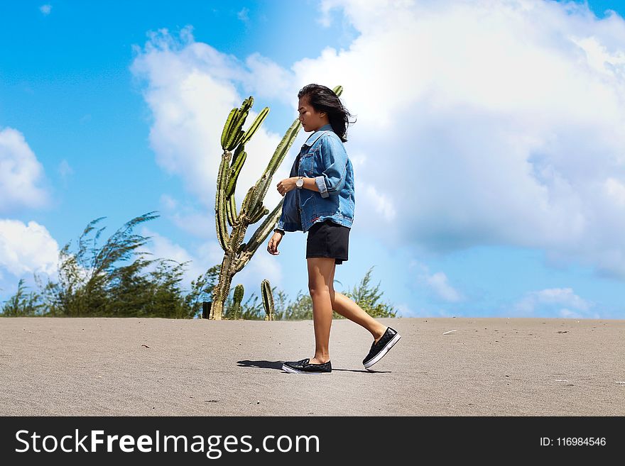 Woman Wearing Chambray Jacket and Black Shorts Walking on Sand Near a Cactus at Daytime