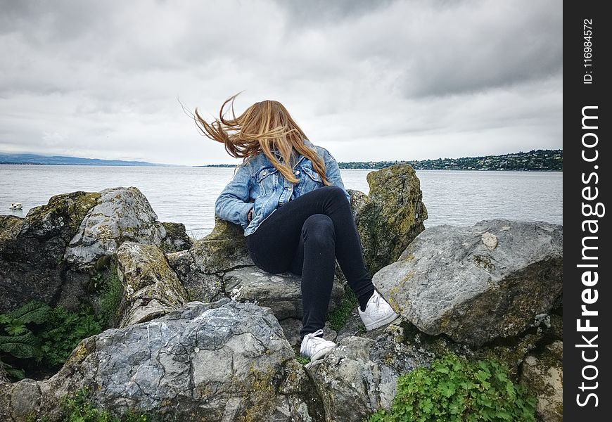 Woman With Blue Denim Collared Button-up Jacket and Black Jeans Sitting on Gray Rock Watching Lakeview