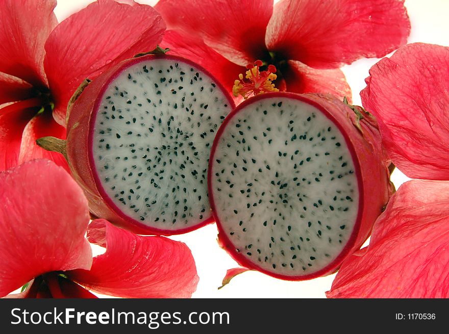 A sliced dragon fruit surrounded by pink hibiscus flowers on a white background. A sliced dragon fruit surrounded by pink hibiscus flowers on a white background