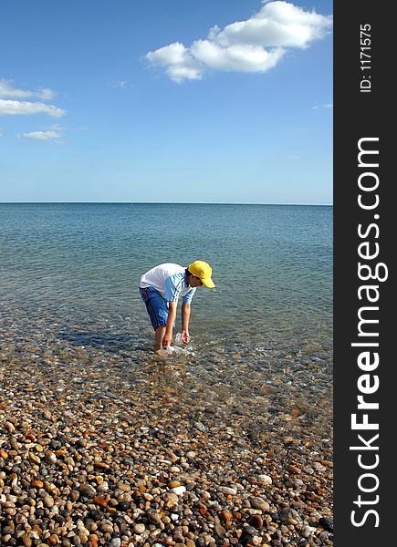 A boy paddling in the sea, pebble beach, calm waters, wide open blue sky