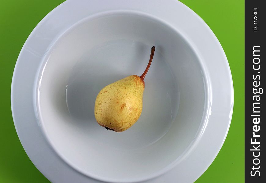 A very little yellow pear lays in a stilish porcelain plate. A plastic green table cloth is the background. A very little yellow pear lays in a stilish porcelain plate. A plastic green table cloth is the background