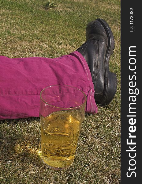 Pint of beer next to someone's leg on grass. Pint of beer next to someone's leg on grass
