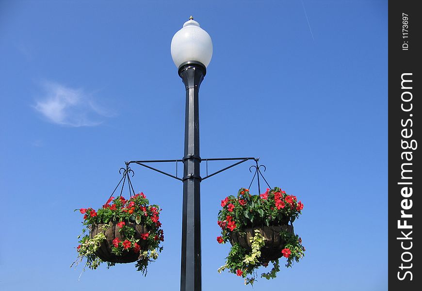 A Lamppost With Two Baskets of Flowers Against a Blue Sky. A Lamppost With Two Baskets of Flowers Against a Blue Sky