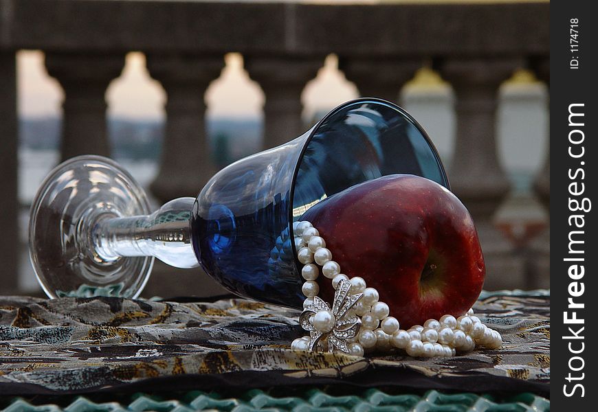 Blue goblet laying on its side with red apple and pearl necklace. Blue goblet laying on its side with red apple and pearl necklace