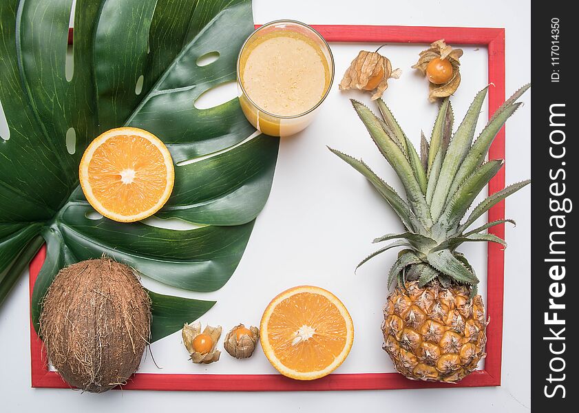 Summer concept, fresh delicious fruit, pineapple, oranges, coconut, orange juice, in a red frame, on a white rustic background, space for text