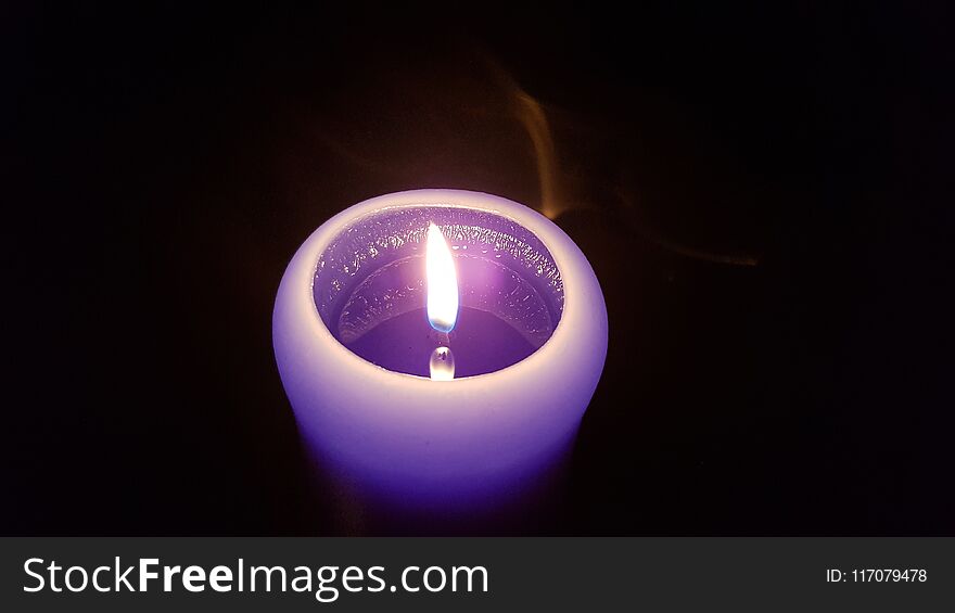 Tiny light of purple candle in the darkness