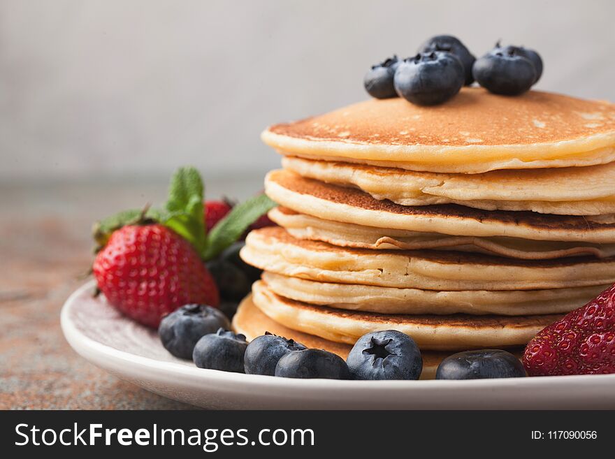 Close-up delicious pancakes, with fresh blueberries, strawberries and maple syrup on a rusty background. With copy space