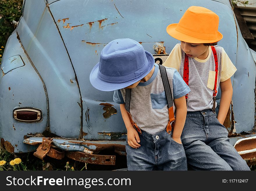 Two Boy in Grey Shirts and Blue Overall Pants Sitting on Blue Car Bumper