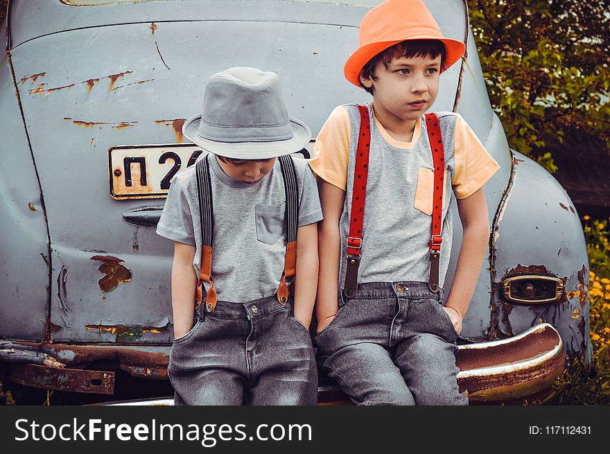 Two Boys Wearing Gray Shirts Sitting on Gray Vehicle Bumper