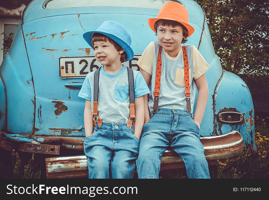 Two Boys Sitting On Classic Blue Car&x27;s Rear Bumper