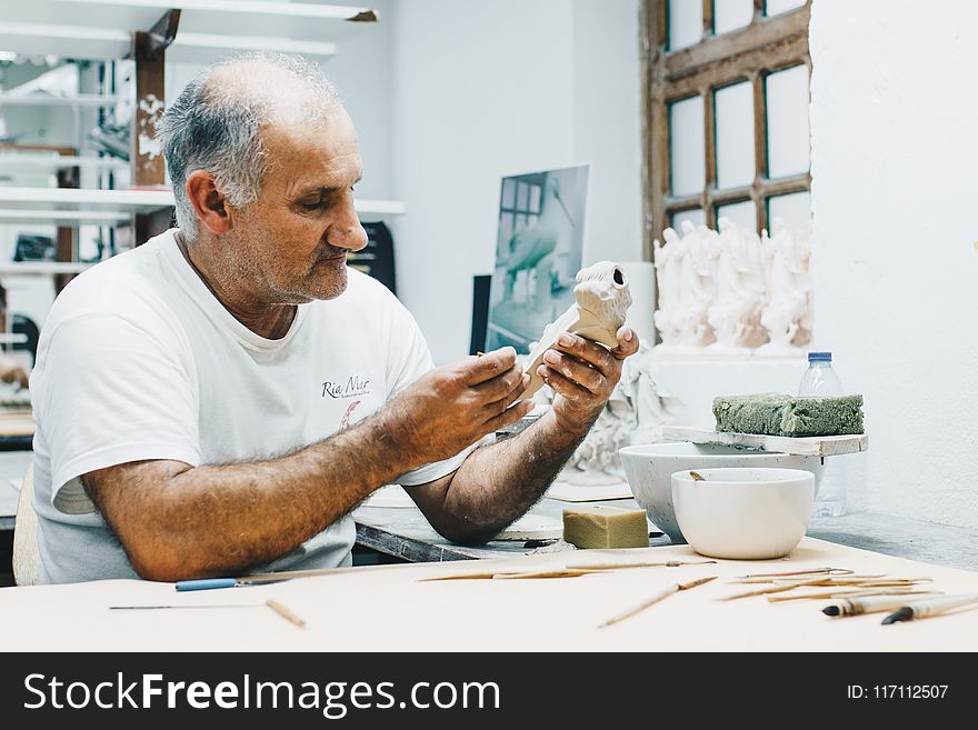 Man in White Crew-neck T-shirt Holding White Figurine