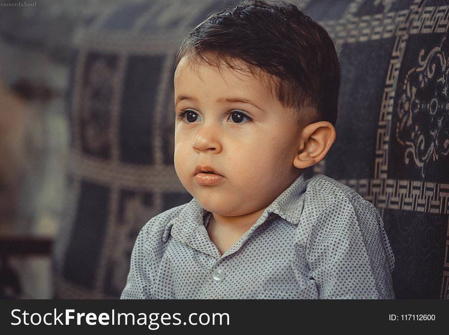 Boy in Gray Button-up Shirt Sitting on Black Sofa