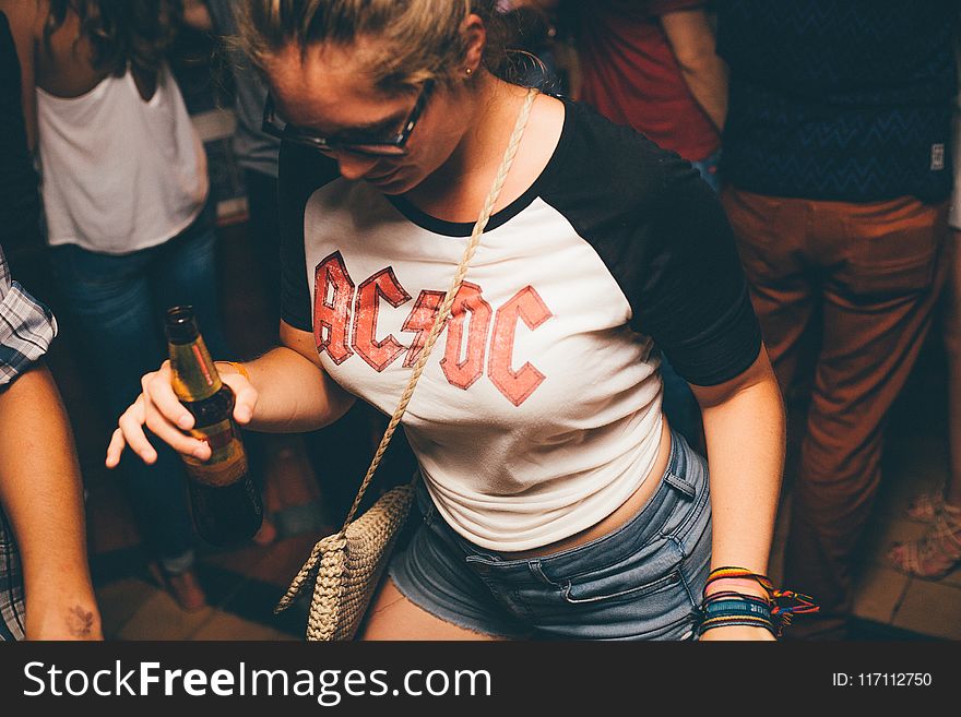 Woman Wearing White and Black Shirt With Acdc Print Holding Brown Glass Bottle