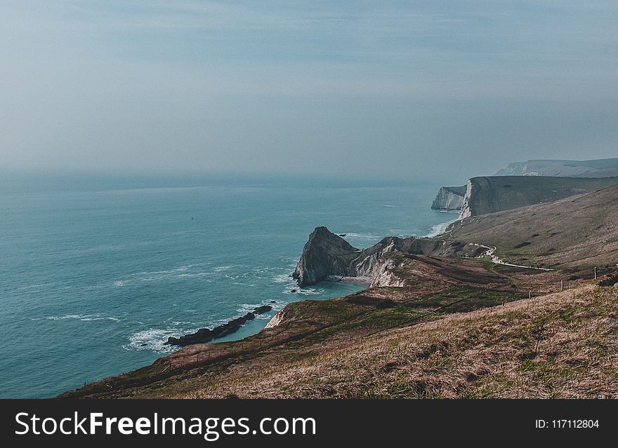 Body Of Water Near Mountain Under Blue Sky At Daytime