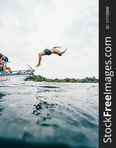 Man Wearing Blue Shorts Performing Back Flip Over Body Of Water