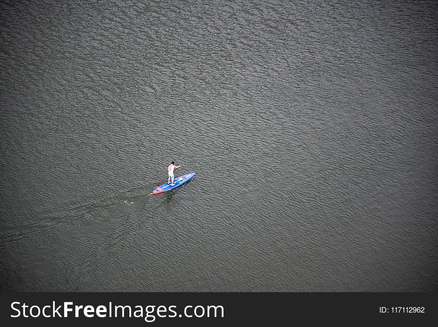 Person Riding Blue and Red Paddleboard on Water