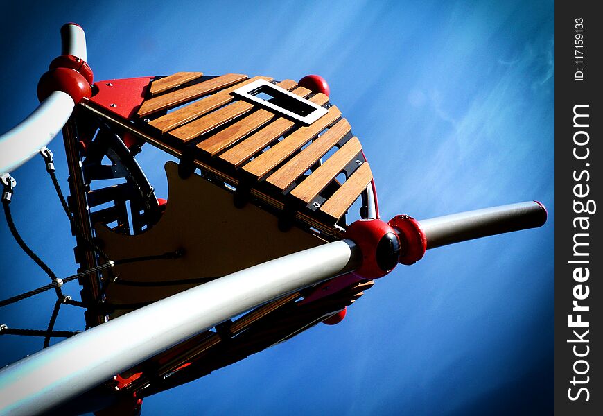 Abstract of modern treehouse in playground with blue sky above with gray steel pipe frame, red ball joints and plastic slats. Abstract of modern treehouse in playground with blue sky above with gray steel pipe frame, red ball joints and plastic slats