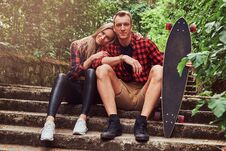 Young Hipster Couple, Handsome Man With A Skateboard And Blonde Girl, Sitting On Steps In A Park. Stock Photo