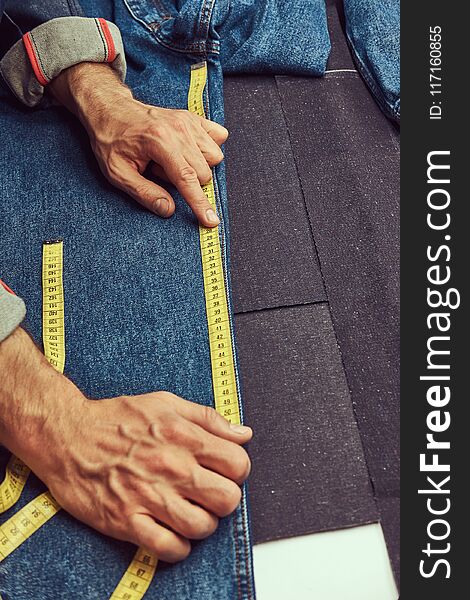 Cropped image of a tailor makes measurements of jeans cloth samples at sewing workshop.