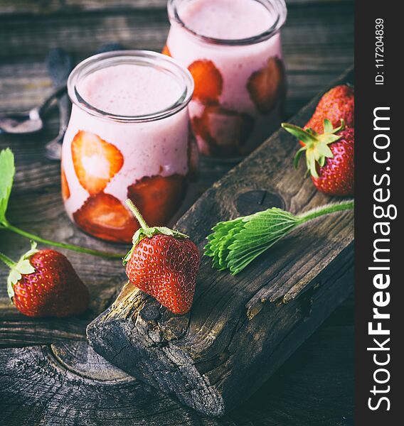 A ripe red strawberry and two glass jars of smoothies on a gray wooden table